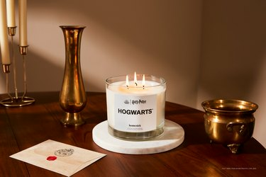 Il Triwick di Hogwarts di Homesick canle su un sottopentola di marmo su un tavolo di legno scuro accanto a una lettera di accettazione di Hogwarts.