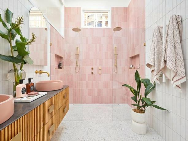 banheiro branco com azulejos rosa no chuveiro e penteadeira de madeira
