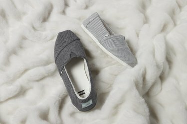 Due pantofole grigie West Elm x TOMS su una coperta bianca