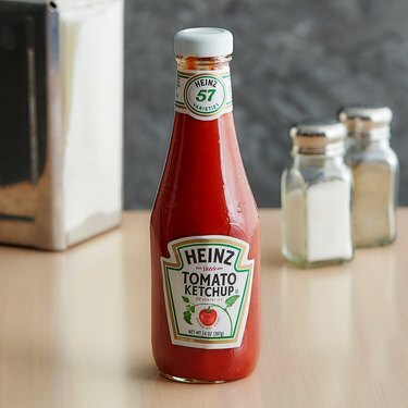 Botella de ketchup Heinz sobre mesa de madera con sal y pimienta