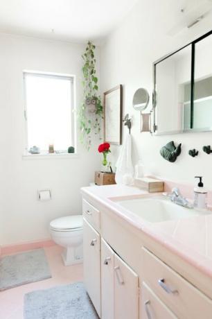 rosa forfengelighet på badet med benkeplate av rosa fliser, undermontert keramisk vask med kran i sølv, rosa flisegulv, hvitt toalett, vindu, rektangulært medisinskap