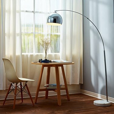 lampada ad arco cromata su tavolo in legno con sedia bianca ispirata agli eames