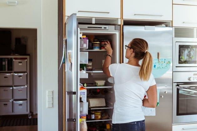 Vista traseira da mulher olhando para a geladeira em pé na cozinha