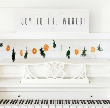 Casa da fazenda Joy to the World com decoração de Natal com placa de lona no piano branco com guirlanda de laranja e zimbro