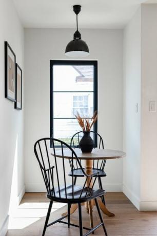 Een raam met zwarte bekleding voor een keukentafel en stoelen