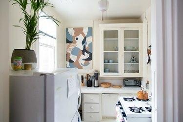 Lite hvitt kjøkken med vindusskap og kunstverk på veggen