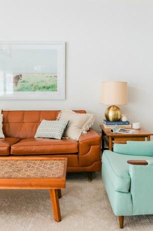 Svetainė su ruda odine sofa, kavos staliuku, šoniniu staliuku ir turkio spalvos akcento kėde