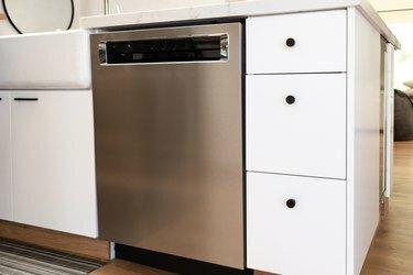 hvide køkkenskabe med sort hardware og rustfri opvaskemaskine