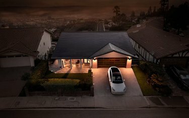 Une maison de style ranch la nuit avec des bardeaux de toit solaires; une Tesla est garée devant