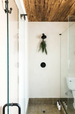chuveiro minimalista branco com piso frio e teto de madeira