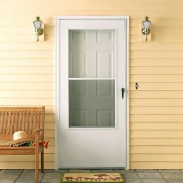 O ușă albă de furtună pe o casă cu tablă galbenă; o bancă stă lângă uşă