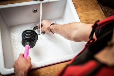 Сантехник с помощью вантуза чинит кухонные раковины
