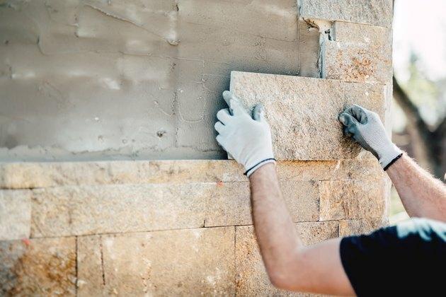 Εργάτης οικοδομών που εγκαθιστά πέτρα στην αρχιτεκτονική πρόσοψη του νέου κτηρίου. λεπτομέρειες της κατασκευαστικής βιομηχανίας