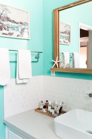 Ideias para organizadores de maquiagem em banheiro com paredes azuis, azulejo branco, espelho, toalheiro, bandeja com loções, maquiagem, pintura, pia branca.