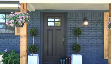 Esterno della casa in mattoni blu navy con finiture nere dei finestrini, porta d'ingresso nera e accenti in legno chiaro.