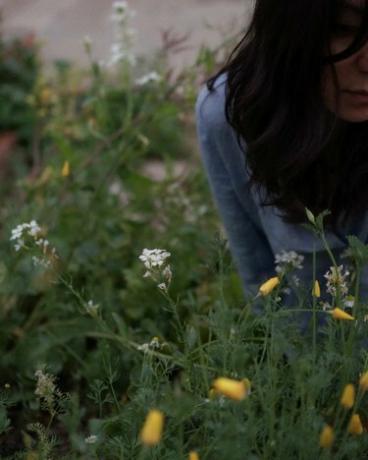 Una persona con lunghi capelli neri in un campo di fiori di campo.