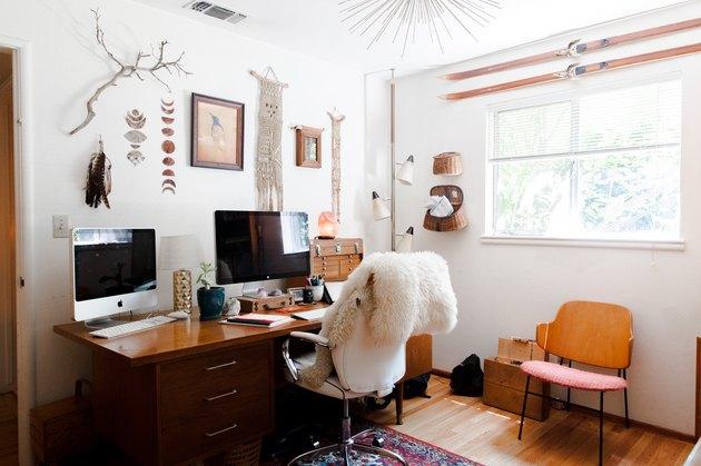 Escritório doméstico com mesa de madeira vintage, decoração de parede boho e janela próxima
