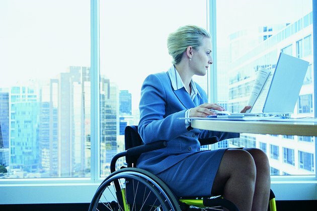 Ofiste bir dizüstü bilgisayar üzerinde çalışan bir tekerlekli sandalyede oturan işkadını