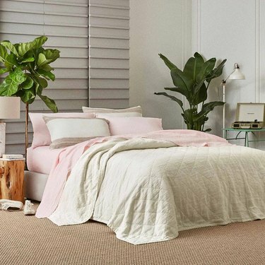Um quarto com roupa de cama e plantas brancas e rosa
