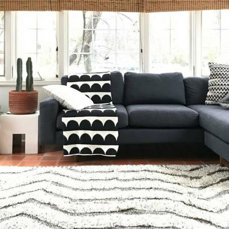 sala de estar com sofá escuro e tapete branco e cobertor preto e branco em cima do sofá