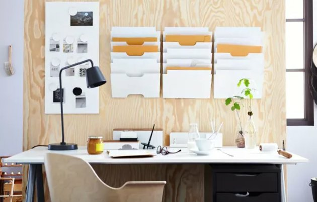 Idéias para organização de home office com parede de madeira compensada com suportes para arquivos suspensos, mesa com lâmpada preta, cadeira de mesa moderna.