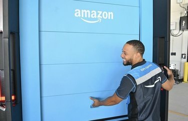 Работник Amazon улыбается за спиной синего грузовика Amazon.