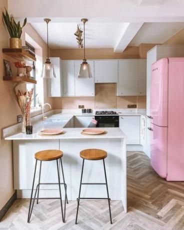 Kapryśna różowa lodówka retro w kuchni z białą zabudową i drewnianymi podłogami w jodełkę