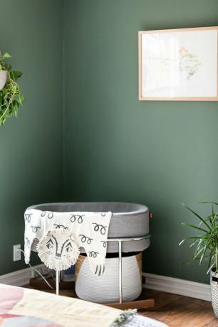 Um viveiro minimalista de paredes verdes com plantas e um berço cinza