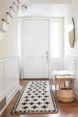 Χρωματισμένο χαλί από γιούτα στην είσοδο δίπλα σε πάγκο, καλάθι και καθρέφτη στον τοίχο.