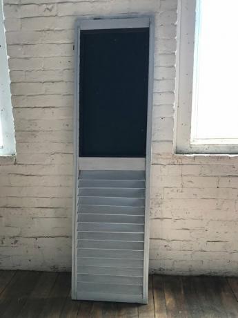 Persiana cinza adaptada com pintura de quadro-negro contra parede de tijolo branco