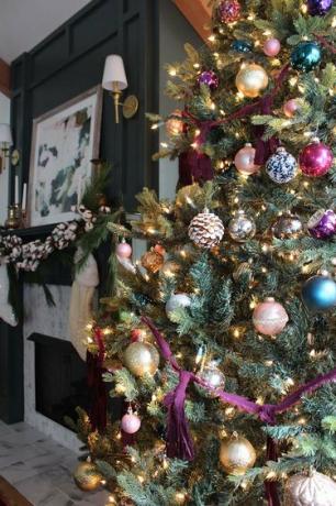 Tamsi svetainė su Kalėdų eglute su violetiniais, pilkais ir auksiniais ornamentais.