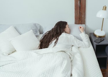 žena koja spava potrbuške u bijelom krevetu pored telefona i lampe na stolu