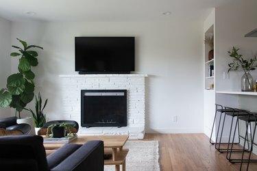 Salón minimalista con muebles modernistas, plantas y tv encima de una chimenea de ladrillo blanco.