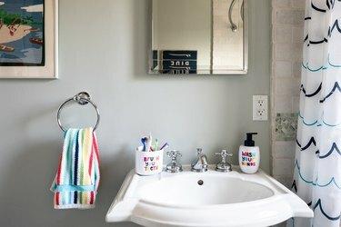 Νεροχύτης βάθρου με τρύπα υπερχείλισης και πολύχρωμη πετσέτα και κουρτίνα μπάνιου