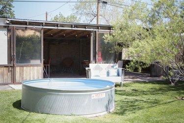 Piscine hors sol argentée devant un grand cabanon en bois et une chaise de patio du milieu du siècle