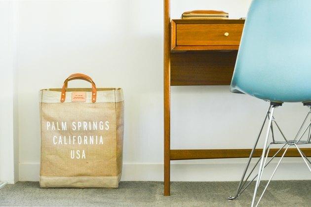 Mesa com cadeira azul e bolsa marrom no chão