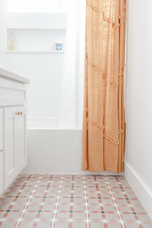 banheiro pequeno com piso de vinil com padrão laranja, preto e branco, penteadeira branca, banheira branca, cortina de chuveiro laranja