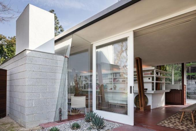 Casa del Mid-Century di John Lautner con travi di legno inclinate e divano vintage con librerie bianche e grandi porte a vetri