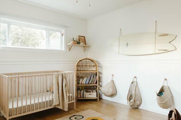 witte minimalistische kinderkamer inrichting met houten wieg en surfplank aan de muur