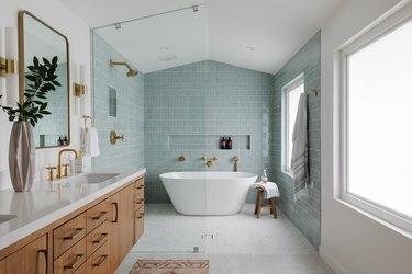 Drėgna kambarys su šviesiai žalsvai mėlynos spalvos plytelėmis, auksinėmis dušo galvutėmis ir vonia