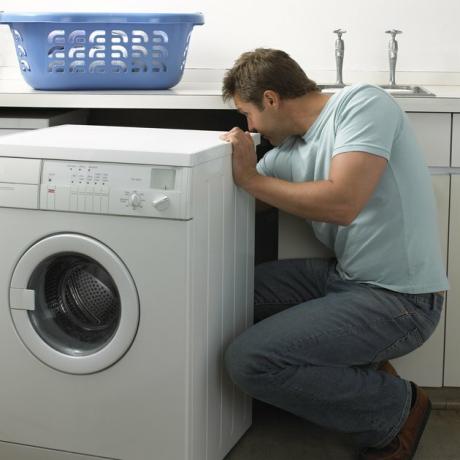 Mann i et kjøkken som reparerer en vaskemaskin