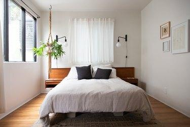 Dormitorio minimalista con cabecero de madera, maceta colgante de macramé y apliques de globo.