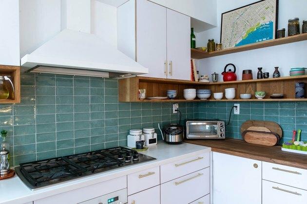 cozinha com backsplash em azulejo azul, cabitnets brancos, exaustor branco e fogão