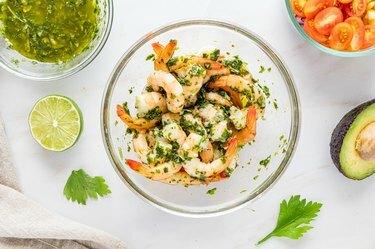 Una ciotola di vetro trasparente con la miscela di gamberi e salsa chimichurri.