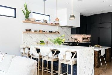 Valkoseinämäinen keittiö, jossa graniittiset tiskit, valkoiset tuolit ja tummanharmaat kaapit