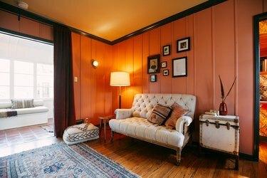 Salon na ranczo z różowymi ścianami, ciemną drewnianą podłogą, wiktoriańską sofą, białym zabytkowym stolikiem do bagażnika z wazonem z piórami