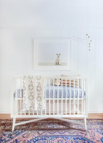 witte minimalistische kinderkamer inrichting met kleurrijke vintage tapijt en witte wieg