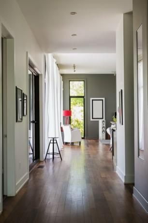 מסדרון עם לוחות רצפה מעץ קומארו. המוביל לסלון עם כורסת עור לבנה, פנים מודרני מפואר בסגנון קובייה