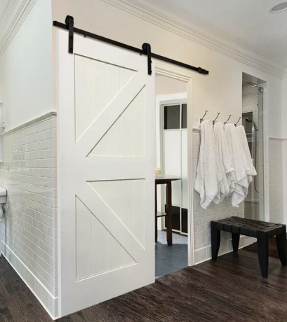 White Contemporary Barn Doors ladrilho de metrô branco, piso de madeira escura, banco de madeira preta, toalhas brancas em ganchos.