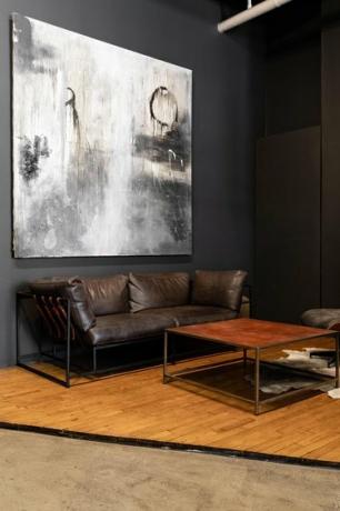 Stue med mørkegrå vægge, et abstrakt maleri, brun lædersofa og firkantet sofabord.
